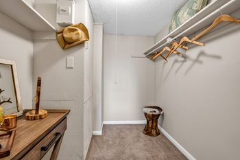 A walk in closet in a bedroom with a large mirror and a wooden stool